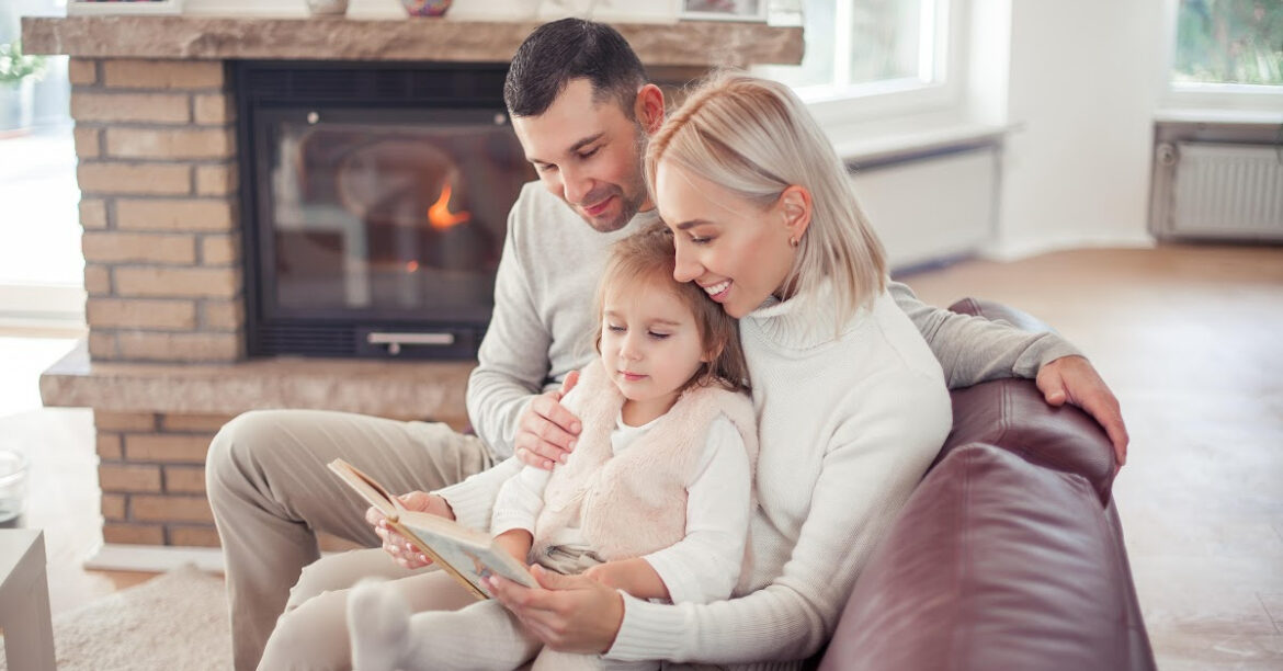 20 Activités Chaleureuses Près du foyer pour le Plaisir et la Détente en Hiver - un couple et leur petite fille lisent un livre au coin du feu