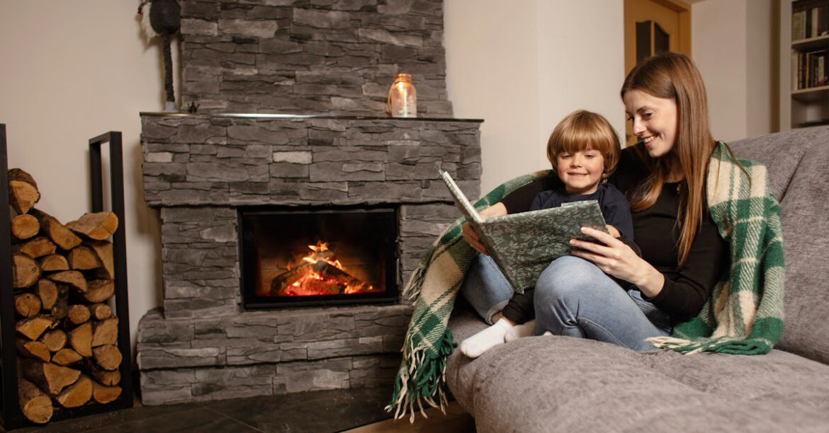 A mother and son cuddle by the fireplace reading a book